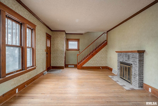 unfurnished living room featuring crown molding, a fireplace, light hardwood / wood-style floors, and a textured ceiling