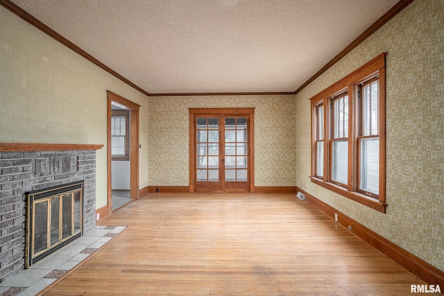 unfurnished living room with french doors, a fireplace, light hardwood / wood-style flooring, and a textured ceiling