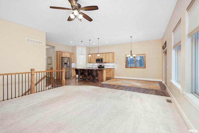 unfurnished living room featuring sink, ceiling fan with notable chandelier, a textured ceiling, and dark colored carpet