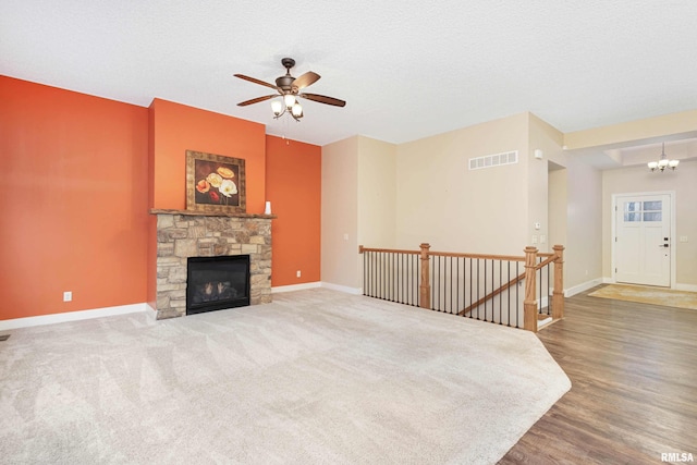 living room featuring ceiling fan with notable chandelier, a stone fireplace, hardwood / wood-style floors, and a textured ceiling