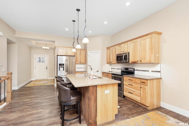 kitchen with sink, appliances with stainless steel finishes, a center island with sink, light brown cabinetry, and decorative light fixtures