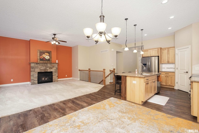 kitchen with hanging light fixtures, a center island with sink, a kitchen bar, light brown cabinetry, and stainless steel fridge with ice dispenser