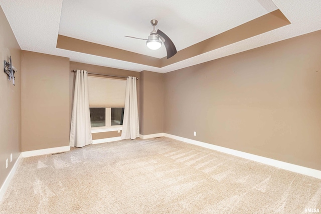 empty room with a raised ceiling, carpet flooring, and ceiling fan