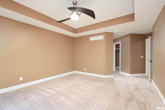 carpeted spare room featuring ceiling fan, a textured ceiling, and a tray ceiling