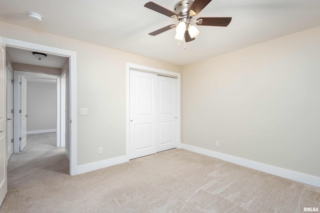 unfurnished bedroom with ceiling fan, light colored carpet, a closet, and a textured ceiling