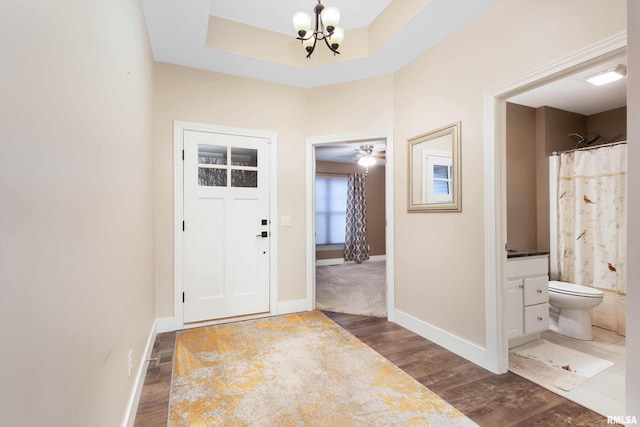 entrance foyer with dark wood-type flooring, an inviting chandelier, and a tray ceiling