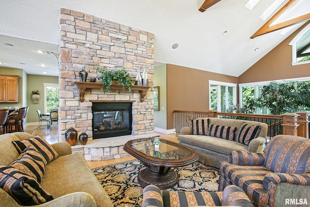 living room with high vaulted ceiling, a fireplace, a skylight, light hardwood / wood-style floors, and beam ceiling