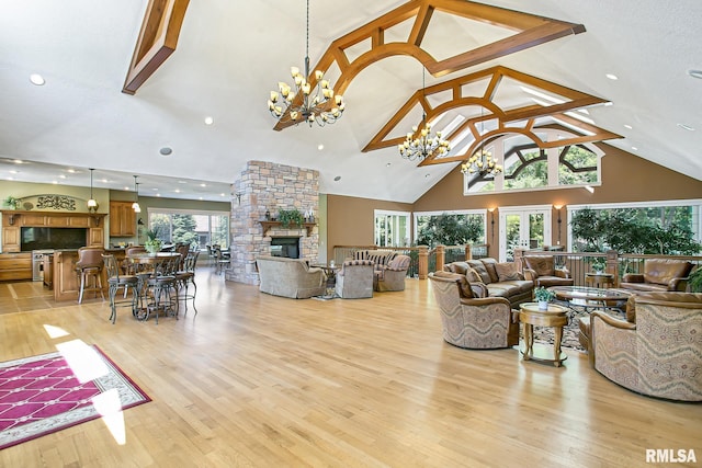 living room featuring high vaulted ceiling, a stone fireplace, light hardwood / wood-style floors, and a chandelier