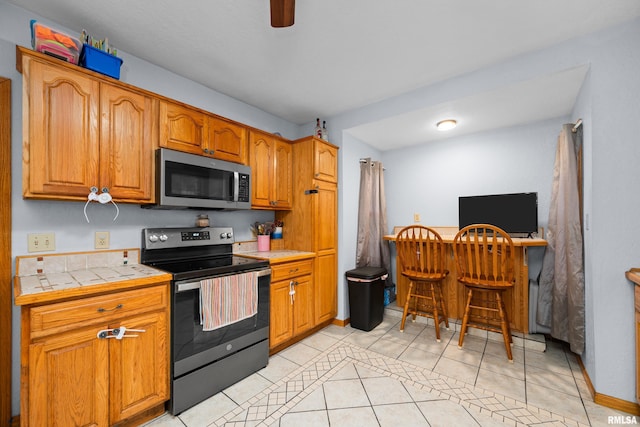 kitchen featuring ceiling fan, tile counters, light tile patterned floors, and electric stove