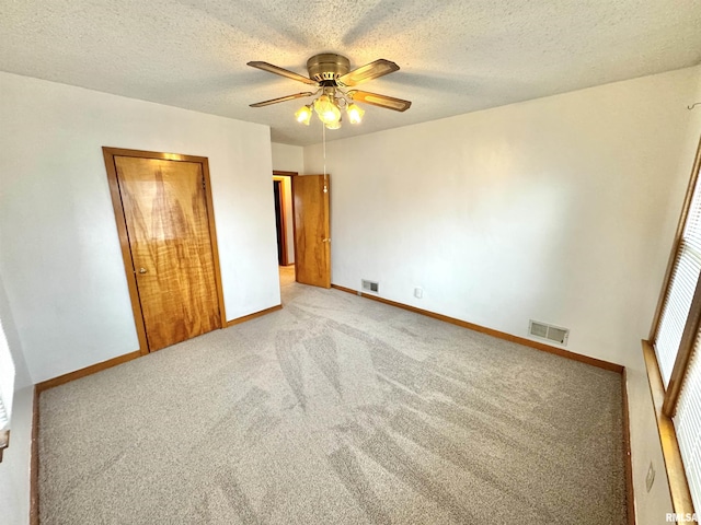 unfurnished bedroom with ceiling fan, light colored carpet, a textured ceiling, and a closet