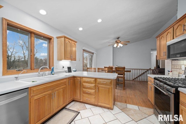 kitchen featuring sink, light tile patterned floors, appliances with stainless steel finishes, vaulted ceiling, and kitchen peninsula