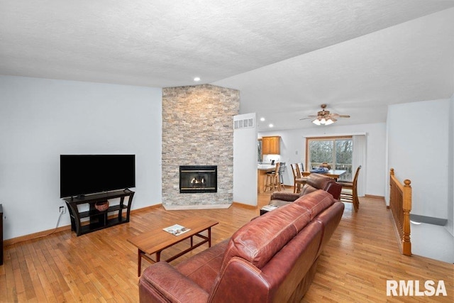 living room with a stone fireplace, lofted ceiling, ceiling fan, light hardwood / wood-style floors, and a textured ceiling