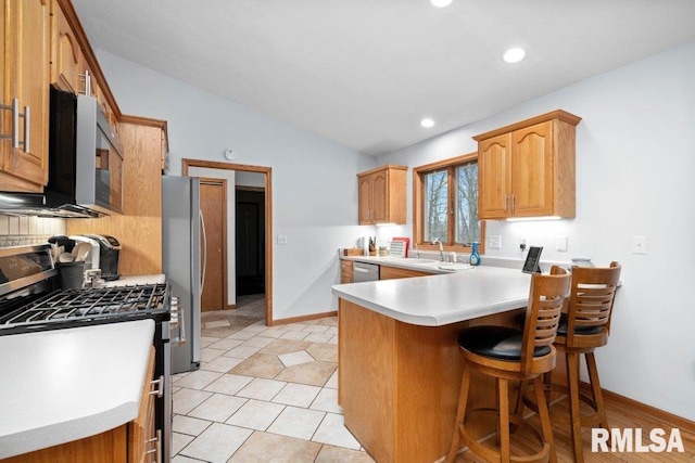 kitchen with lofted ceiling, sink, a kitchen breakfast bar, stainless steel appliances, and kitchen peninsula