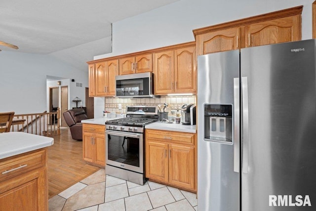 kitchen featuring lofted ceiling, tasteful backsplash, light tile patterned flooring, and appliances with stainless steel finishes