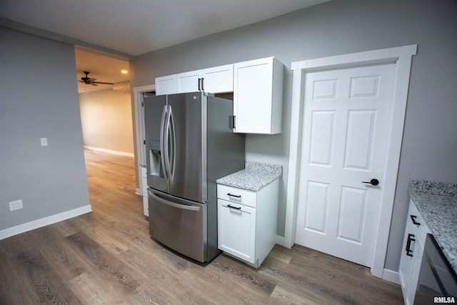 kitchen with stainless steel fridge with ice dispenser, white cabinetry, hardwood / wood-style flooring, ceiling fan, and light stone counters