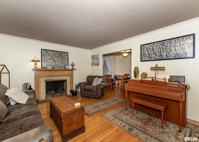 living room featuring crown molding, a brick fireplace, and light wood-type flooring