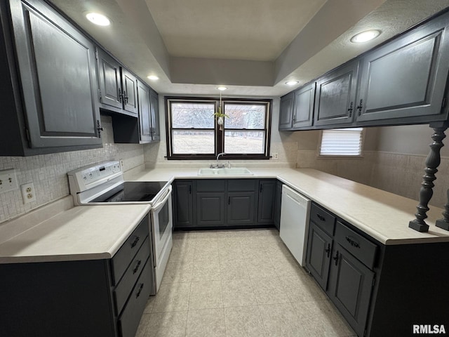 kitchen featuring white appliances, a tray ceiling, sink, and decorative backsplash