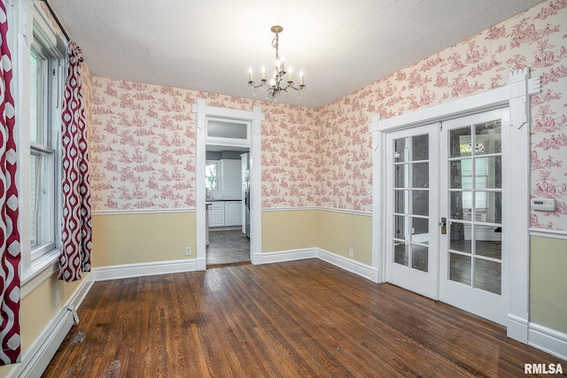 empty room with french doors, an inviting chandelier, a textured ceiling, dark hardwood / wood-style flooring, and a baseboard heating unit