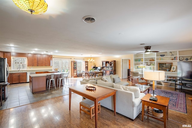 living room featuring ceiling fan with notable chandelier, sink, and light hardwood / wood-style flooring