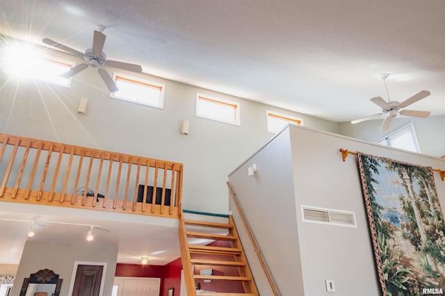 stairs with rail lighting, ceiling fan, and a high ceiling