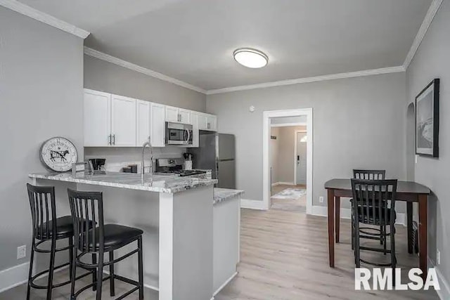 kitchen with white cabinetry, a kitchen breakfast bar, kitchen peninsula, stainless steel appliances, and crown molding