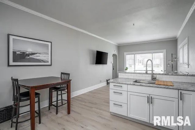 kitchen featuring white cabinetry, sink, ornamental molding, and light wood-type flooring