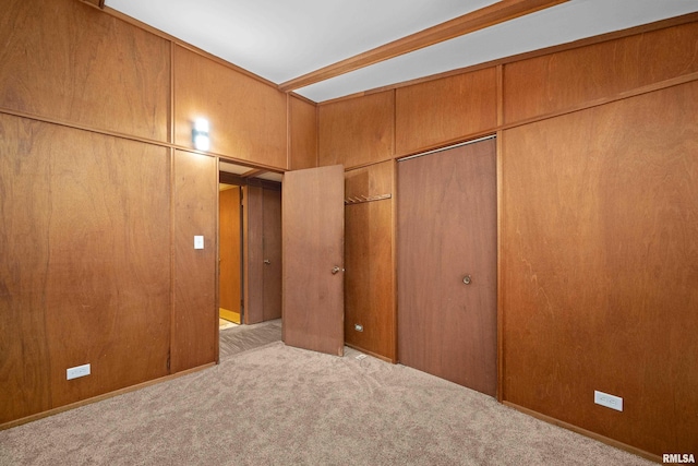 unfurnished bedroom featuring light colored carpet, a closet, and wood walls