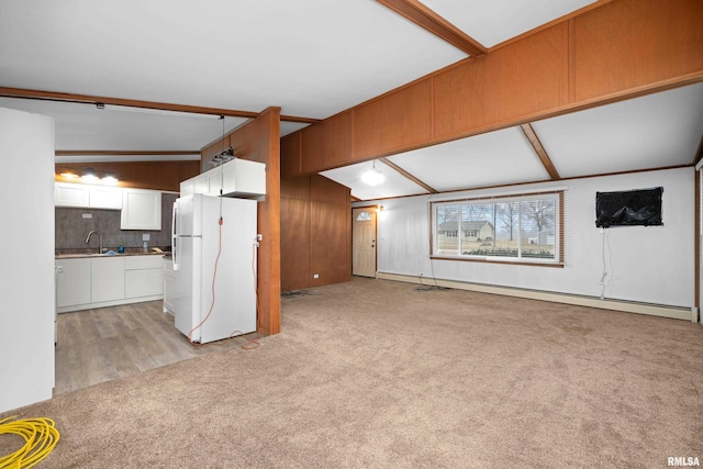 unfurnished living room with sink, vaulted ceiling with beams, wooden walls, light colored carpet, and a baseboard heating unit