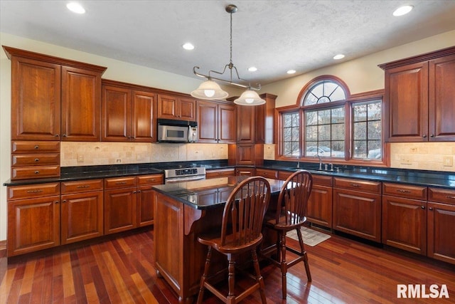 kitchen with dark wood-type flooring, a breakfast bar, appliances with stainless steel finishes, a center island, and decorative light fixtures