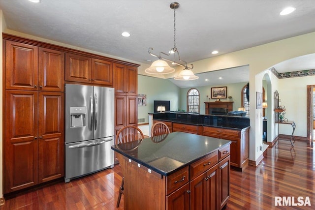 kitchen with stainless steel refrigerator with ice dispenser, dark wood-type flooring, a breakfast bar area, a center island, and hanging light fixtures