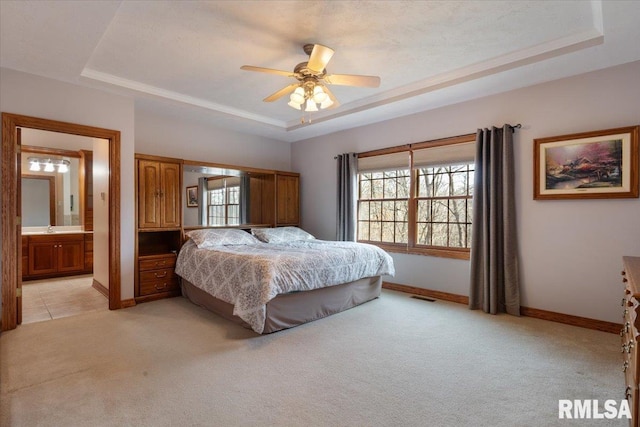 bedroom with ceiling fan, light colored carpet, ensuite bath, and a tray ceiling