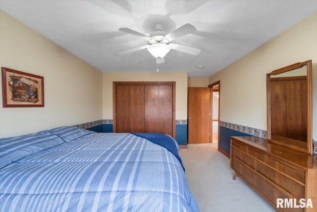 bedroom featuring ceiling fan, light colored carpet, a closet, and a textured ceiling