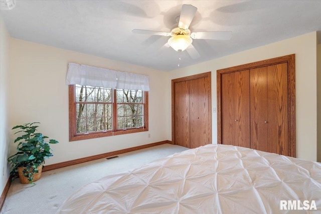 unfurnished bedroom featuring ceiling fan, light carpet, and two closets