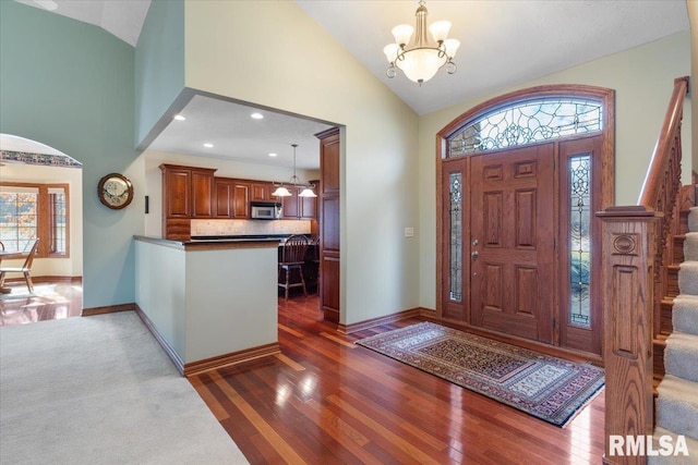 foyer featuring an inviting chandelier, high vaulted ceiling, dark wood-type flooring, and a wealth of natural light