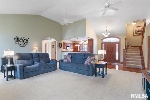 carpeted living room featuring high vaulted ceiling and ceiling fan with notable chandelier