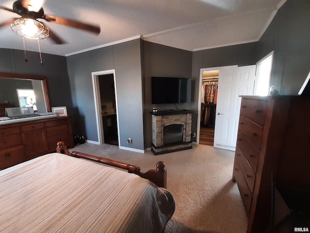 bedroom with ceiling fan, a fireplace, ornamental molding, light carpet, and a spacious closet