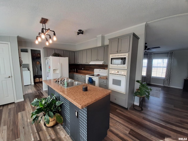 kitchen featuring white appliances, dark wood-type flooring, hanging light fixtures, an island with sink, and washer / dryer