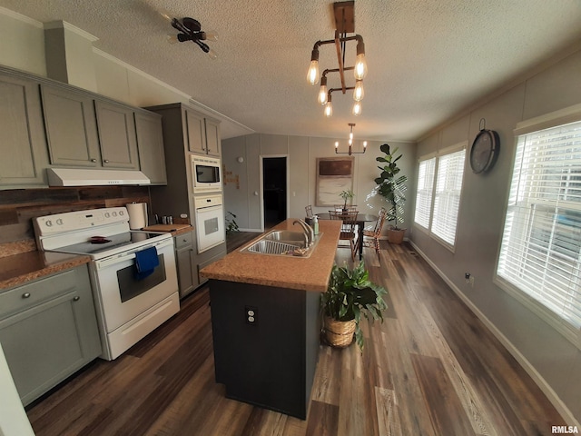 kitchen featuring sink, decorative light fixtures, a chandelier, a center island with sink, and white appliances