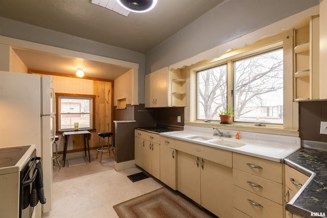 kitchen featuring white electric stove, sink, wooden walls, and cream cabinetry