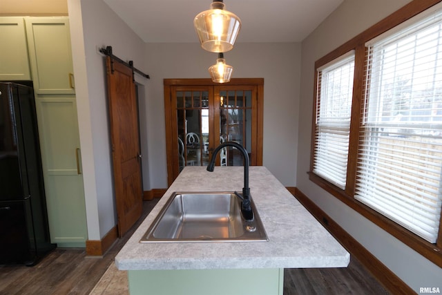 kitchen with decorative light fixtures, an island with sink, sink, black fridge, and a barn door