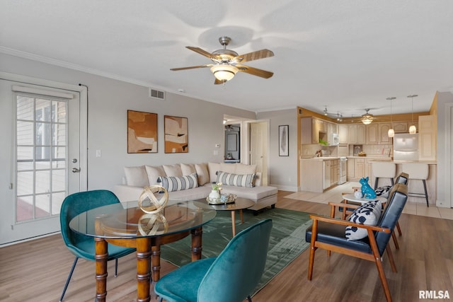 living room with ceiling fan, ornamental molding, and light wood-type flooring