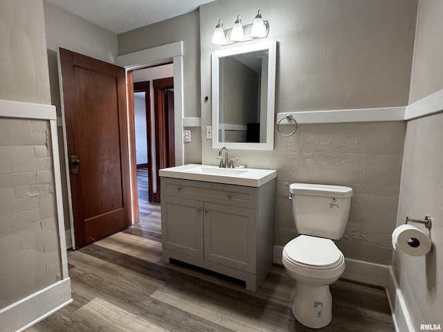 half bath featuring a textured ceiling, vanity, toilet, and wood finished floors