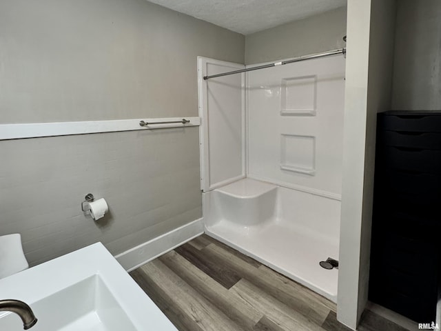 bathroom with a stall shower, a textured ceiling, baseboards, and wood finished floors