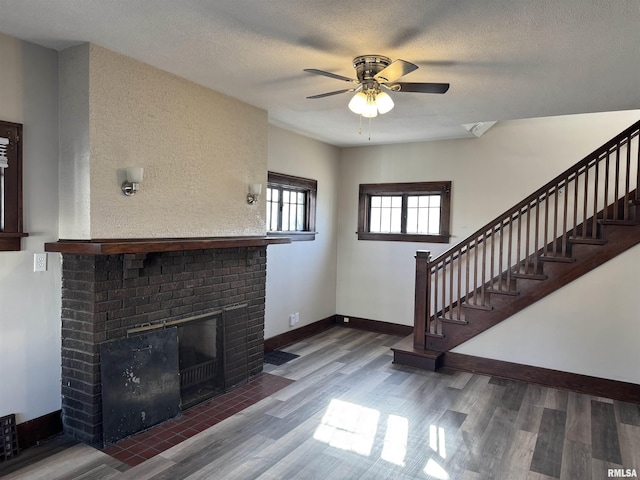 unfurnished living room with a fireplace, stairway, a textured ceiling, wood finished floors, and baseboards