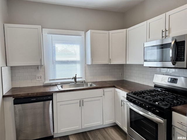 kitchen featuring stainless steel appliances, butcher block countertops, wood finished floors, a sink, and white cabinetry