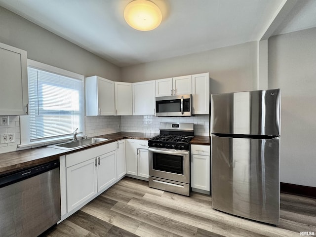 kitchen featuring stainless steel appliances, tasteful backsplash, wooden counters, light wood-style floors, and a sink