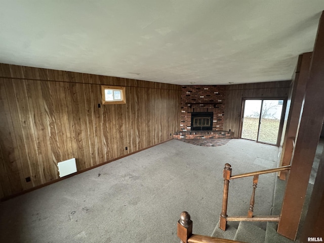 unfurnished living room with a brick fireplace, carpet, and wooden walls