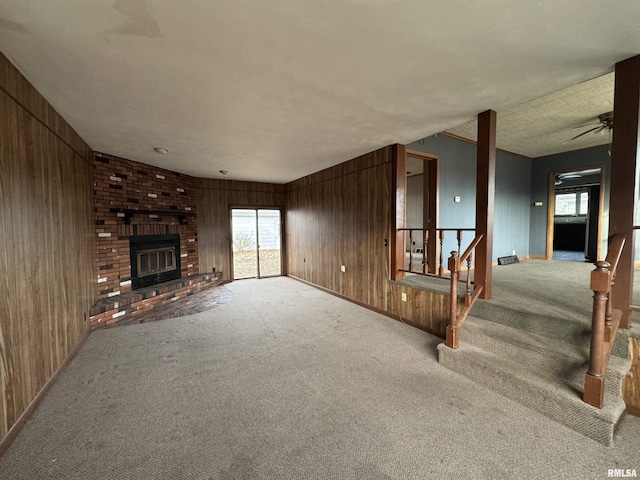 unfurnished living room featuring a brick fireplace, wooden walls, and light colored carpet