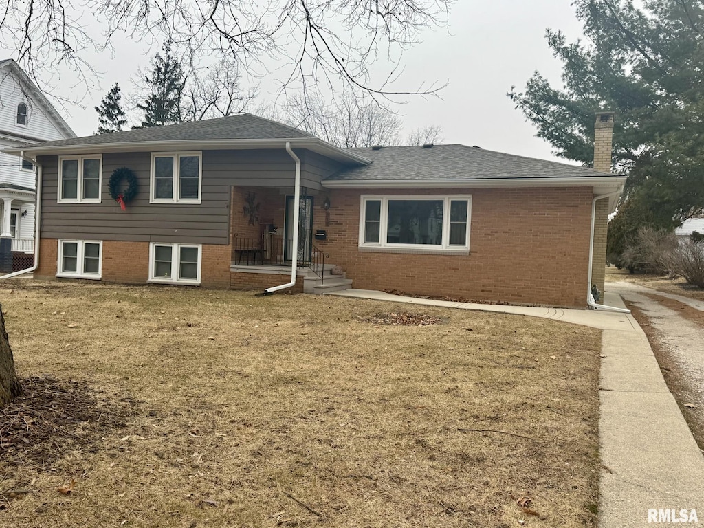 split level home with roof with shingles, brick siding, a chimney, and a front yard