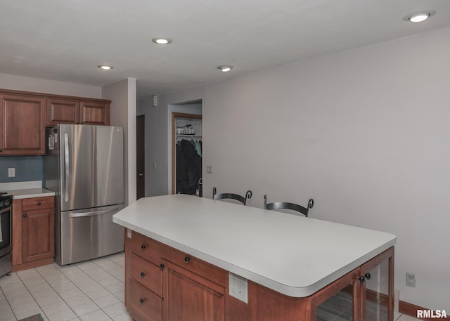 kitchen featuring stove, a center island, light tile patterned floors, and stainless steel refrigerator